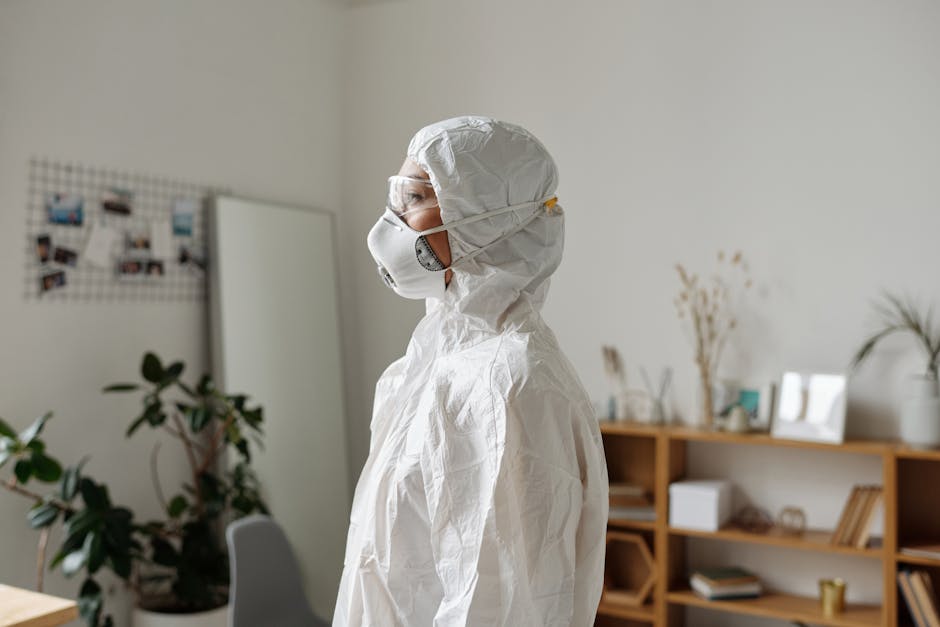 A healthcare worker in full protective PPE gear inside a room with plants and shelves.