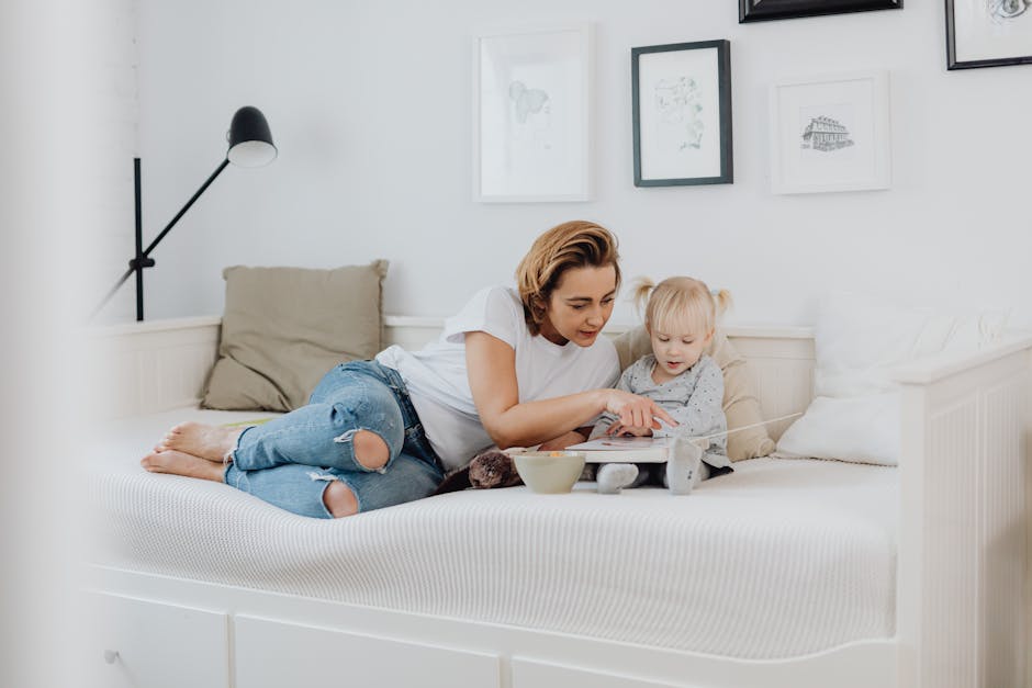 A mother and daughter enjoy quality time reading together in a sunlit bedroom.