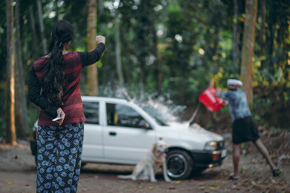 A family scene of washing a car outdoors in a wooded area. Includes a dog.