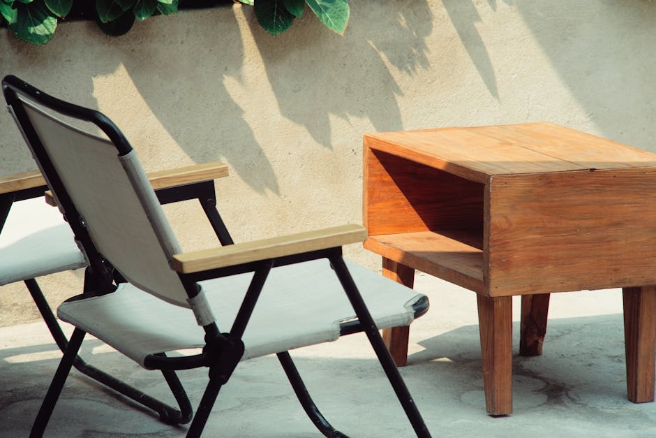 A relaxing patio scene featuring a wooden coffee table and folding chair in natural sunlight.